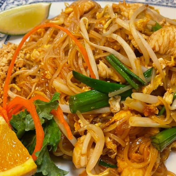 A close-up of Pad Thai noodles with chicken, bean sprouts, green onions, and a lime wedge.