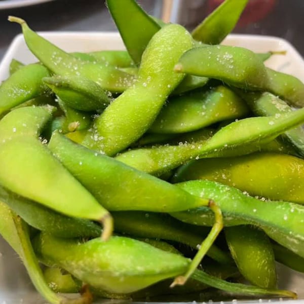 A close-up of bright green edamame pods, lightly salted, served in a white bowl.