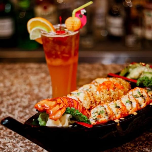 Sushi Naiya's sushi boat with lobster, rolls, and a tropical cocktail on a bar.
